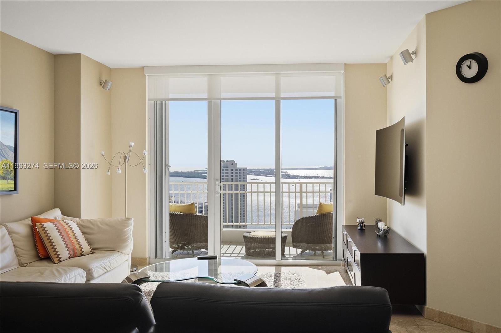A living room features a glass coffee table, a balcony with water views, and a television — 801 Brickell Key Blvd # 3209, Miami FL 33131, MIAMI, FL