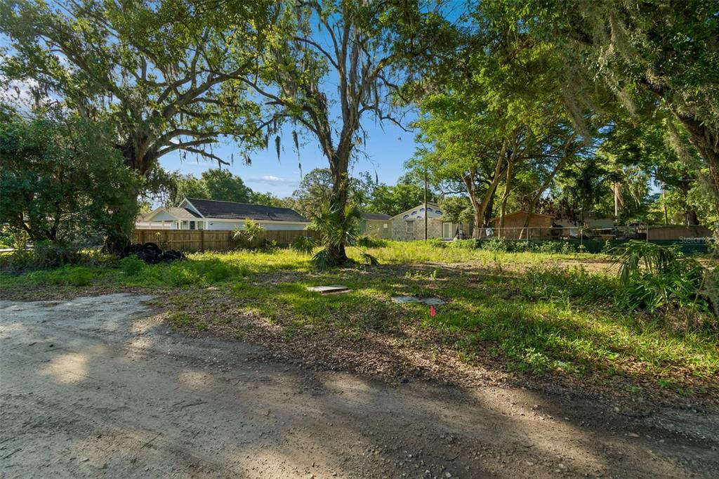 A vacant, grassy lot with mature trees and a dirt road in the foreground — 1401 DRANE STREET SE, PLANT CITY, FL