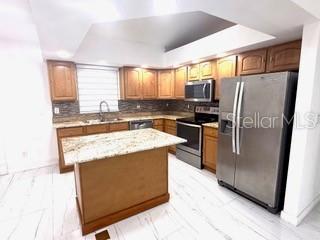 A kitchen with wooden cabinets, a granite-topped island, stainless steel appliances, and white tiled floors — 313 NW 16TH PLACE, CAPE CORAL, FL