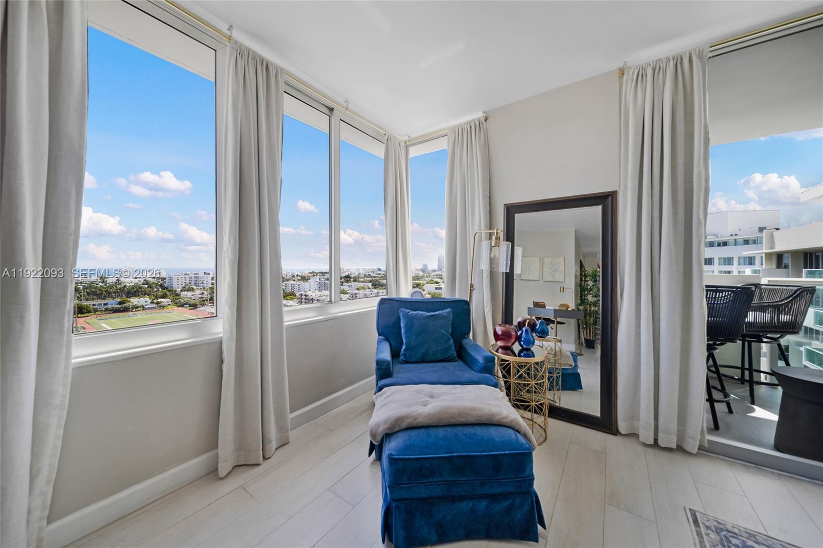 A sunlit corner room features a blue chaise lounge, floor-to-ceiling windows, and a balcony — 1200 West Ave # 15, Miami Beach FL 33139, MIAMI BEACH, FL