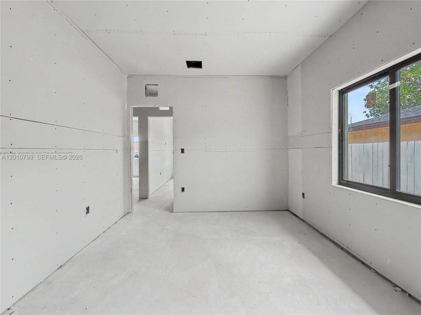 An unfinished room features bare drywall, a concrete floor, and a window looking outdoors — 640 SW 10th Ave, Homestead FL 33030, HOMESTEAD, FL