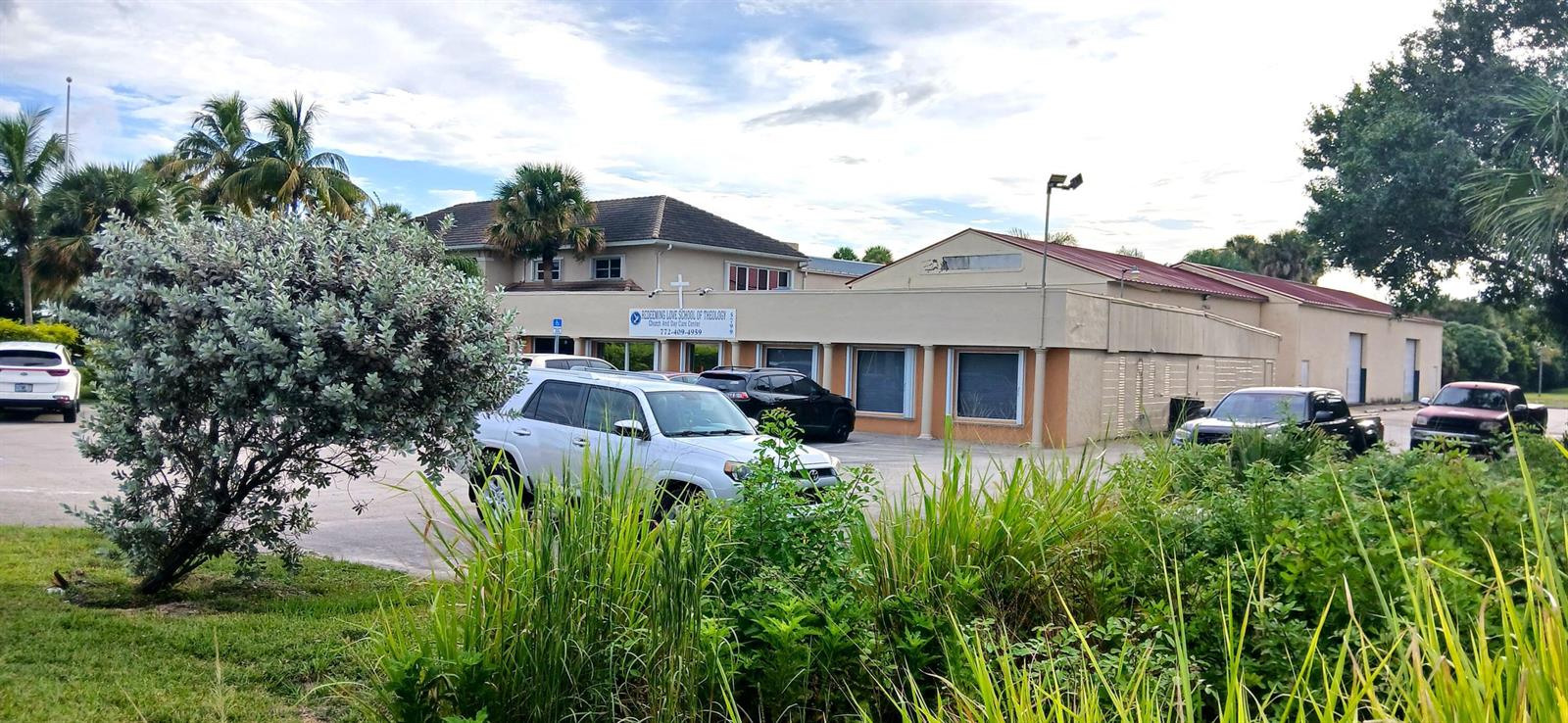 A low-rise commercial building with a parking lot and surrounding landscaping under a cloudy sky — 0000 S Us-1, Fort Pierce FL 34982, FORT PIERCE, FL