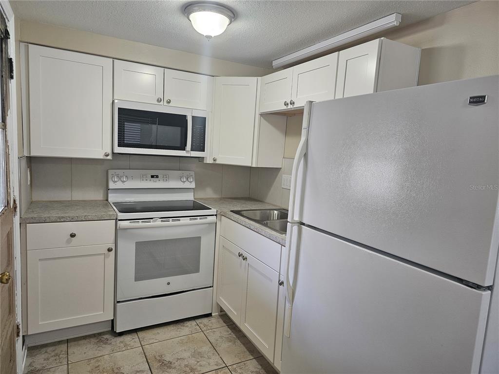 A kitchen features white cabinets, white appliances, a tiled floor, and a laminate countertop — 5603 CHEYENNE DRIVE, HOLIDAY, FL