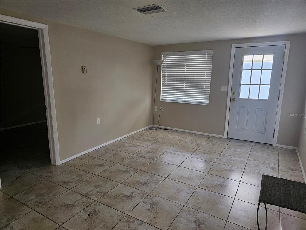 An empty room features beige walls, light-colored tile flooring, a window with blinds, and a door — 5603 CHEYENNE DRIVE, HOLIDAY, FL