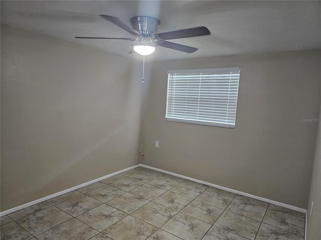 An empty room features beige walls, a ceiling fan, and light-colored square floor tiles — 5603 CHEYENNE DRIVE, HOLIDAY, FL