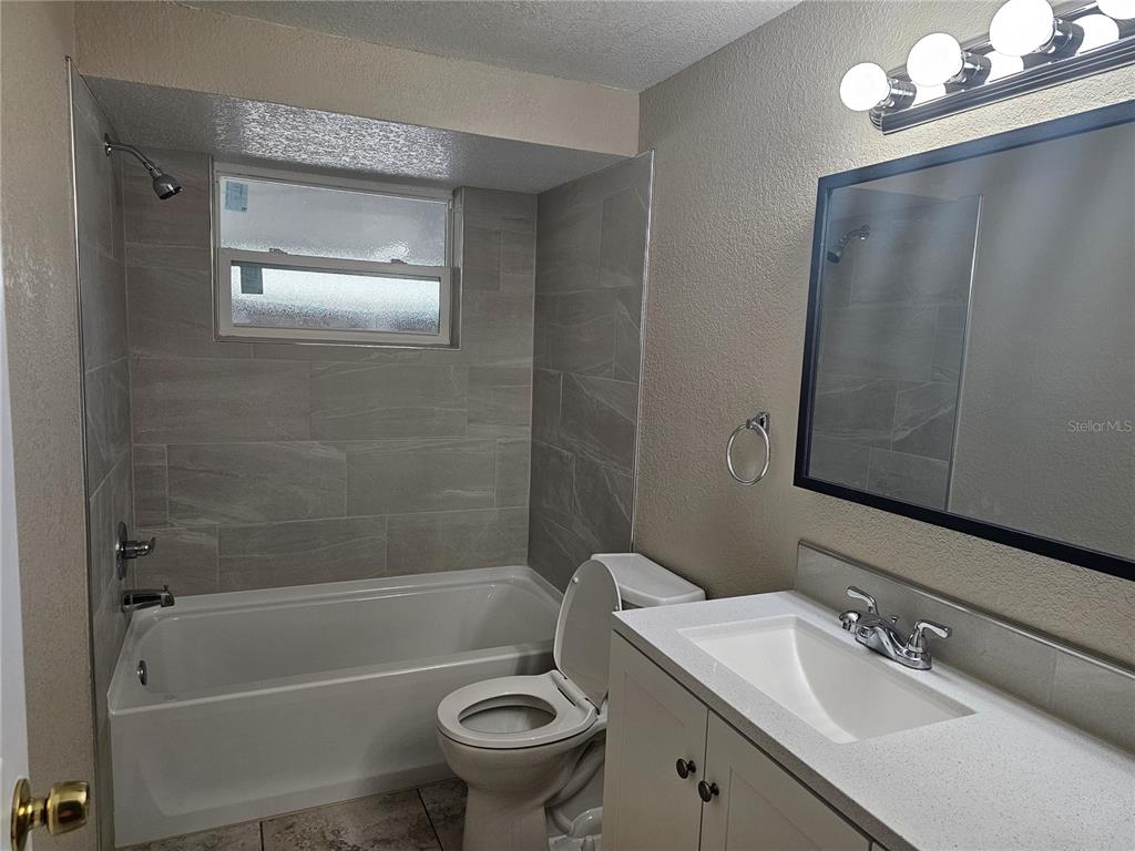 A bathroom features a tiled bathtub shower combo, a toilet, and a white vanity — 5603 CHEYENNE DRIVE, HOLIDAY, FL