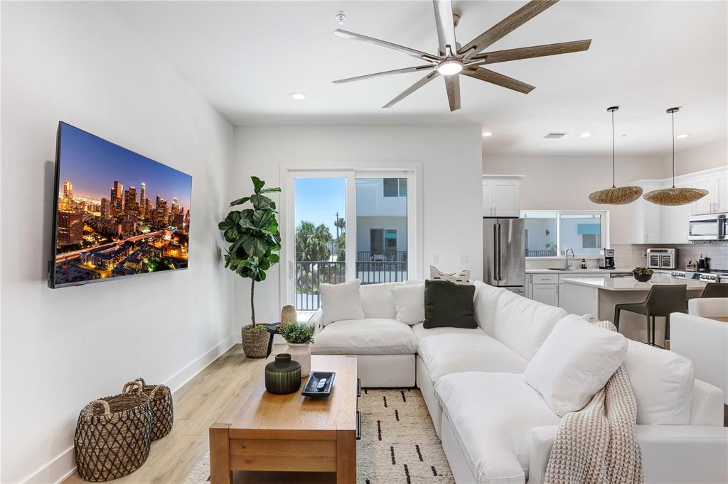 A modern living room features a white sectional sofa, wood coffee table, and wall-mounted television — 15405 GULF BOULEVARD UNIT B4, ST PETERSBURG, FL