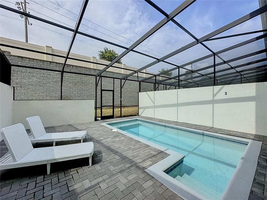 A rectangular swimming pool with lounge chairs sits inside a screened-in patio enclosure — 267 JETTY WAY, DAVENPORT, FL