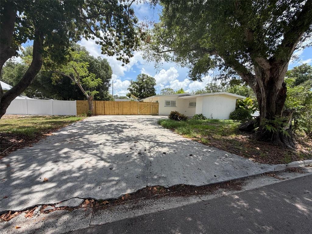 A concrete driveway leads to a single-story house with a white fence and large trees — 2612 9TH, BRADENTON, FL