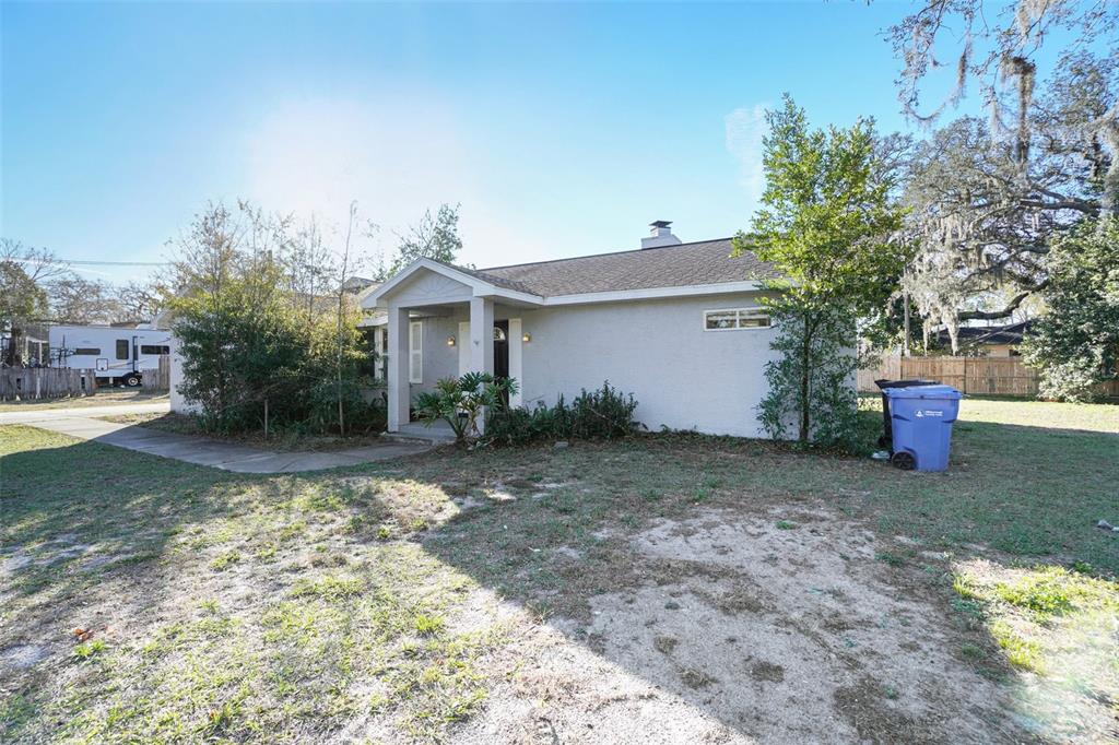 A single-story house with a covered entryway, light-colored stucco exterior, and a blue trash bin — 13210 MAPLE STREET, ODESSA, FL