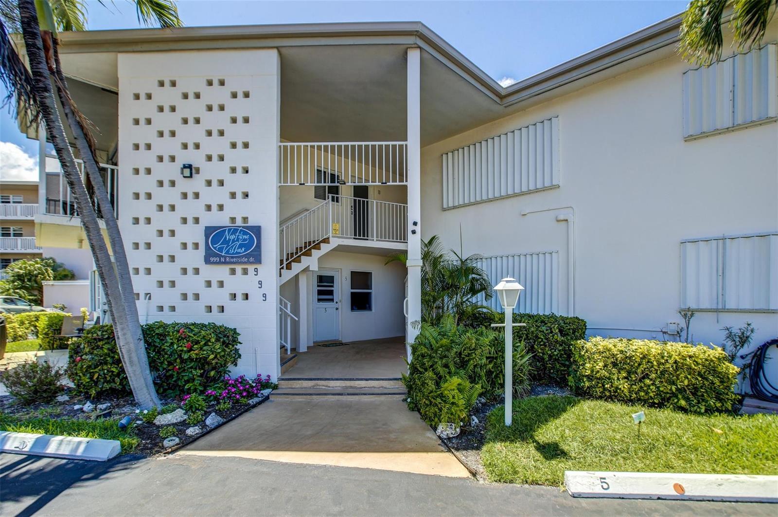 The exterior of a two-story apartment building features a white facade, stairs, and landscaping — 999 N Riverside Drive # 11, Pompano Beach FL 33062, POMPANO BEACH, FL