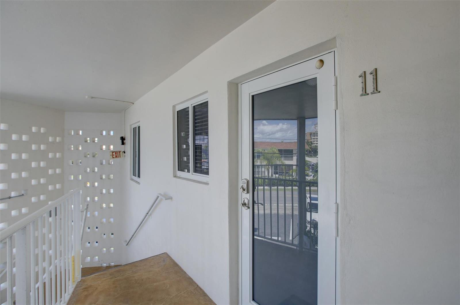 A white exterior hallway features a door numbered 11, a window, and a stairwell — 999 N Riverside Drive # 11, Pompano Beach FL 33062, POMPANO BEACH, FL