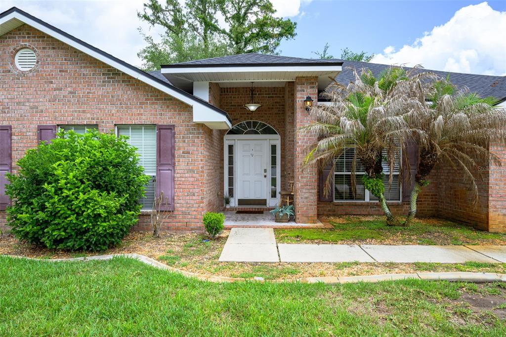 A brick house exterior features a covered entryway, a white front door, and a palm tree — 11 RIDDLE DRIVE, PALM COAST, FL
