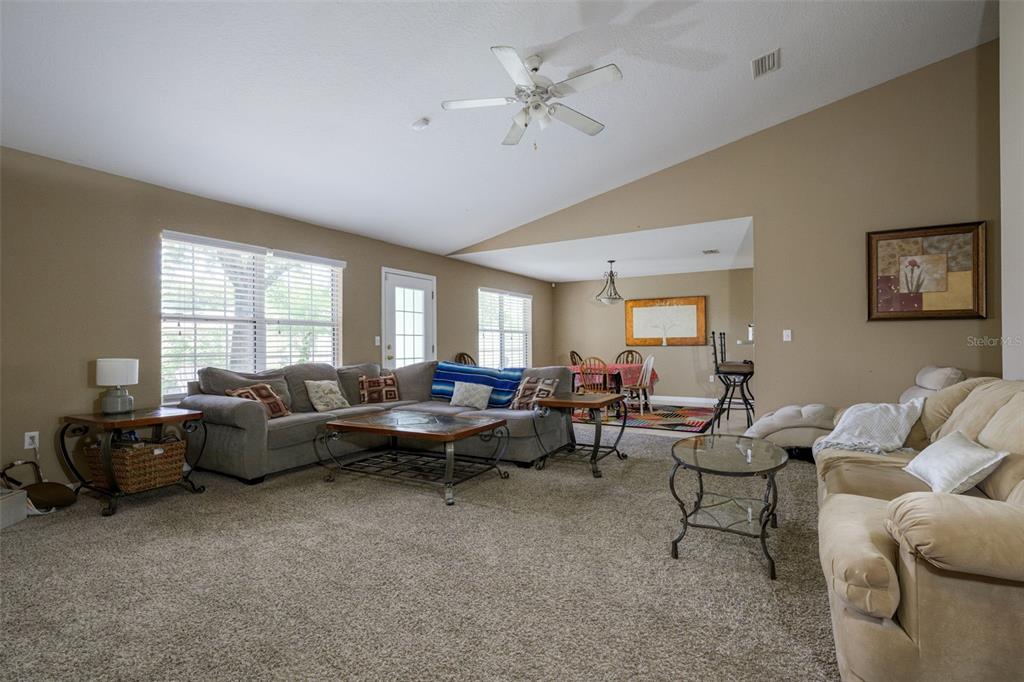 A living room with beige carpet, vaulted ceilings, and a dining area in the background — 11 RIDDLE DRIVE, PALM COAST, FL