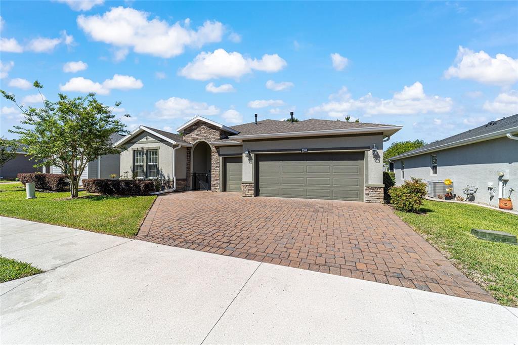 A single-story house with a stone-accented facade, a brick paver driveway, and a three-car garage — 3584 NW 56TH AVENUE, OCALA, FL