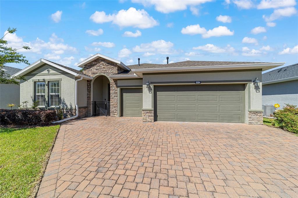 A single-story house features a stone-accented entryway, a paver driveway, and a three-car garage — 3584 NW 56TH AVENUE, OCALA, FL