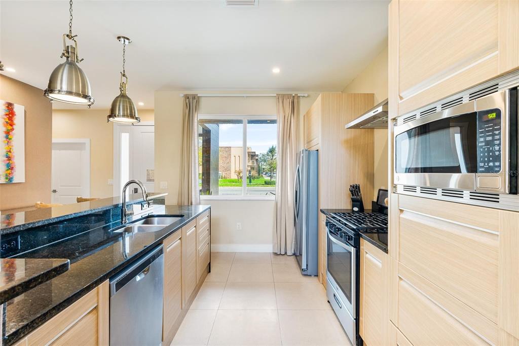 A modern kitchen features light wood cabinetry, black granite countertops, and stainless steel appliances — 3167A BRASILIA AVENUE, KISSIMMEE, FL