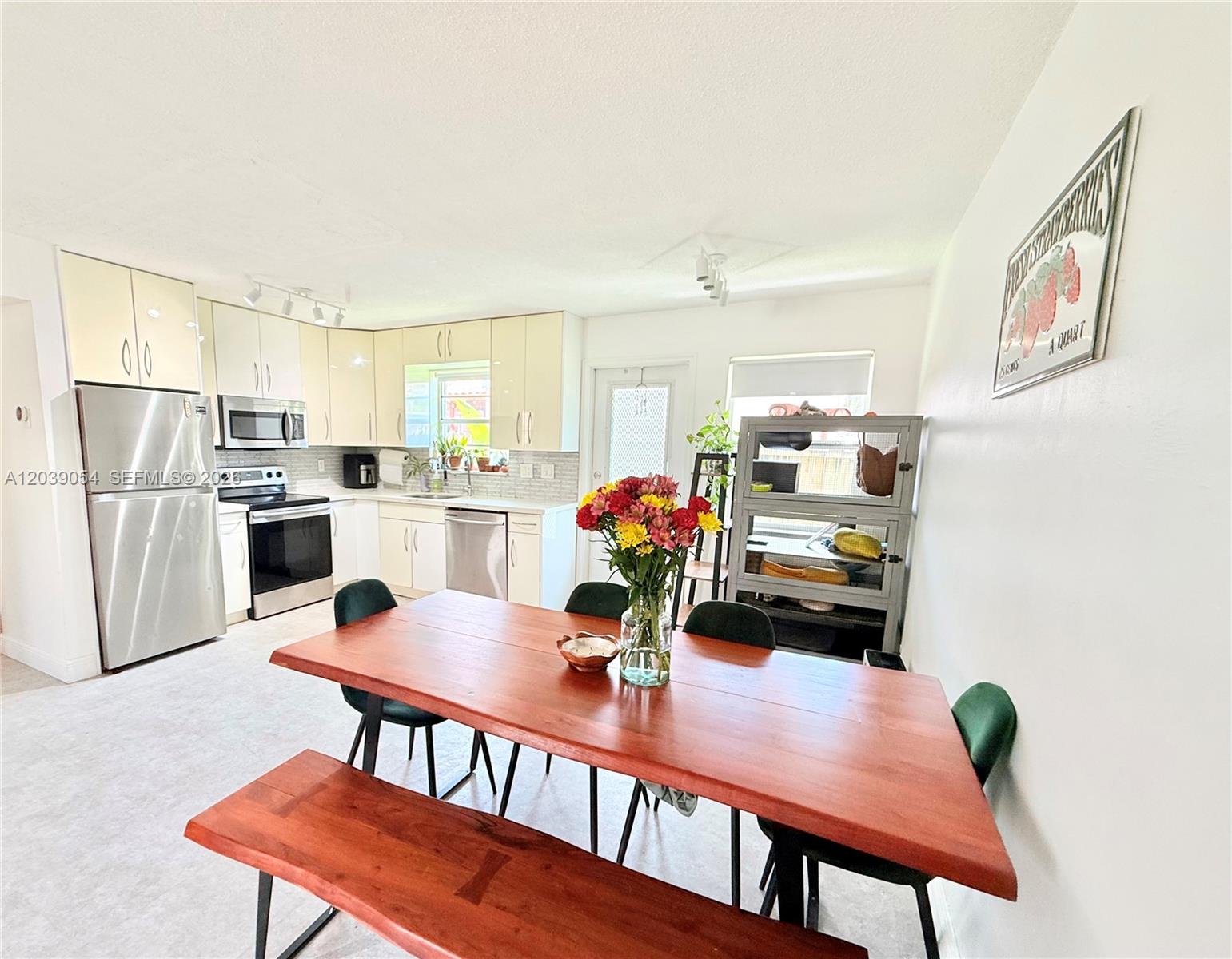 A kitchen with light-colored cabinets and stainless steel appliances opens to a wooden dining area — 1722 Mayo St # 105, Hollywood FL 33020, HOLLYWOOD, FL