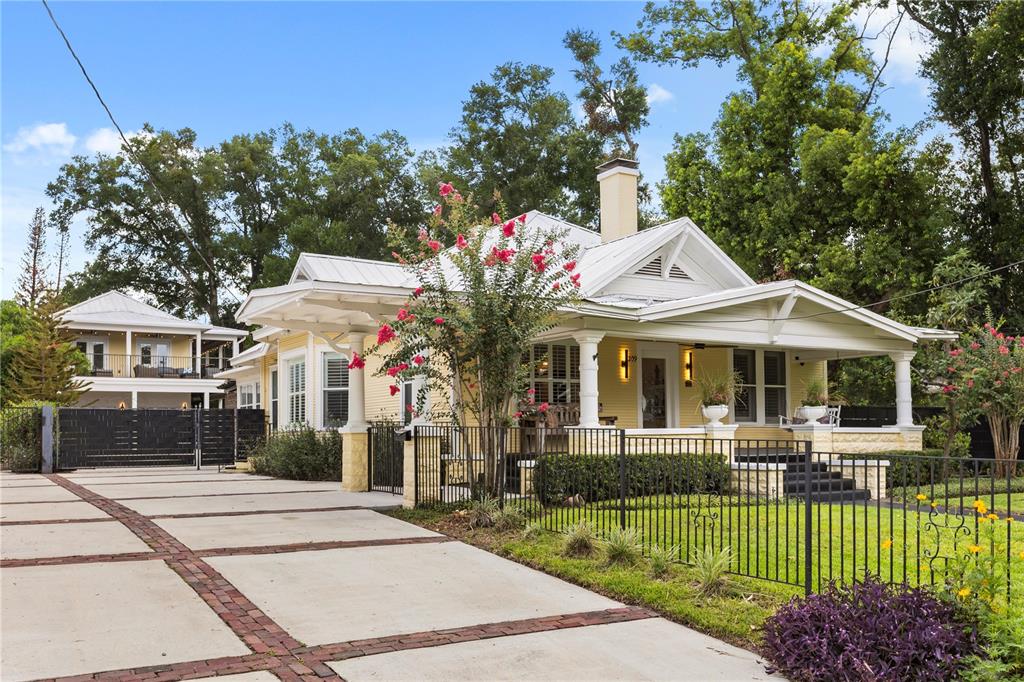 A yellow bungalow with a metal roof and a large concrete driveway sits behind fencing — 209 E AMELIA STREET, ORLANDO, FL