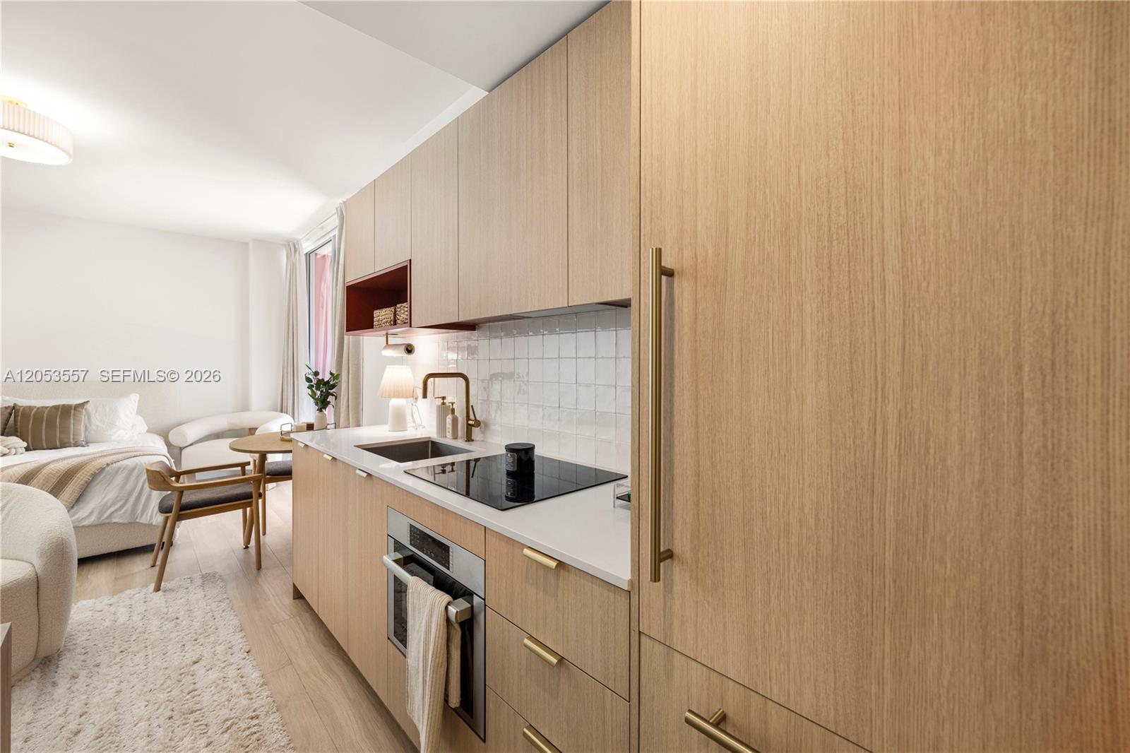 A modern kitchenette features light wood cabinetry, a white tiled backsplash, and integrated appliances — 90 NE 32 St # 715, Miami FL 33127, MIAMI, FL