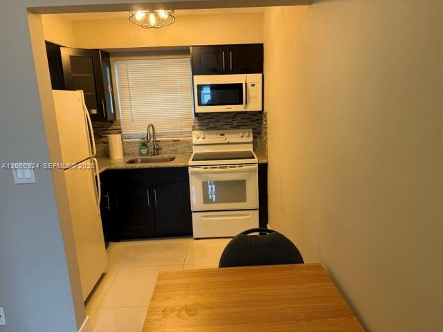 A kitchen features dark cabinets, white appliances, a tiled backsplash, and a light-colored floor — 1859 Wiley St # 3, Hollywood FL 33020, HOLLYWOOD, FL