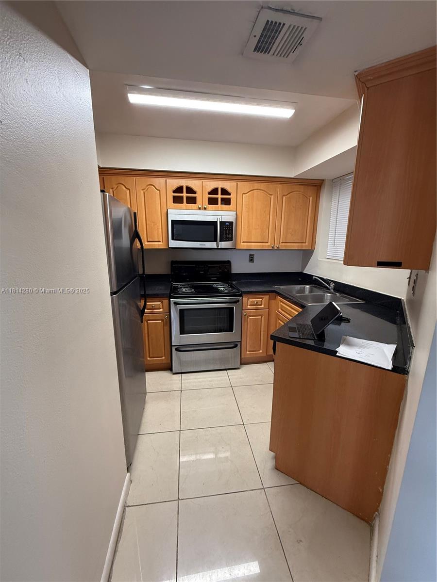A kitchen features light wood cabinets, stainless steel appliances, black countertops, and light-colored tile flooring — 8255 SW 152 AV # 2, Miami FL 33193, MIAMI, FL
