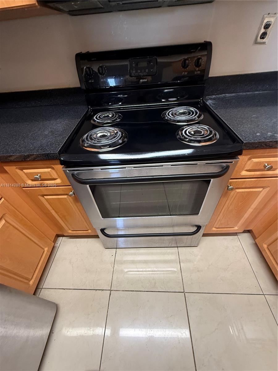 A stainless steel electric range is situated between wooden cabinets and dark countertops — 8255 SW 152 AV # 2, Miami FL 33193, MIAMI, FL