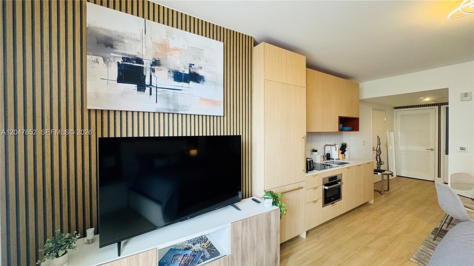 A modern studio apartment features a kitchenette, a wall-mounted television, and wood-slat accent wall paneling — 90 NE 32 St # 613, Miami FL 33137, MIAMI, FL