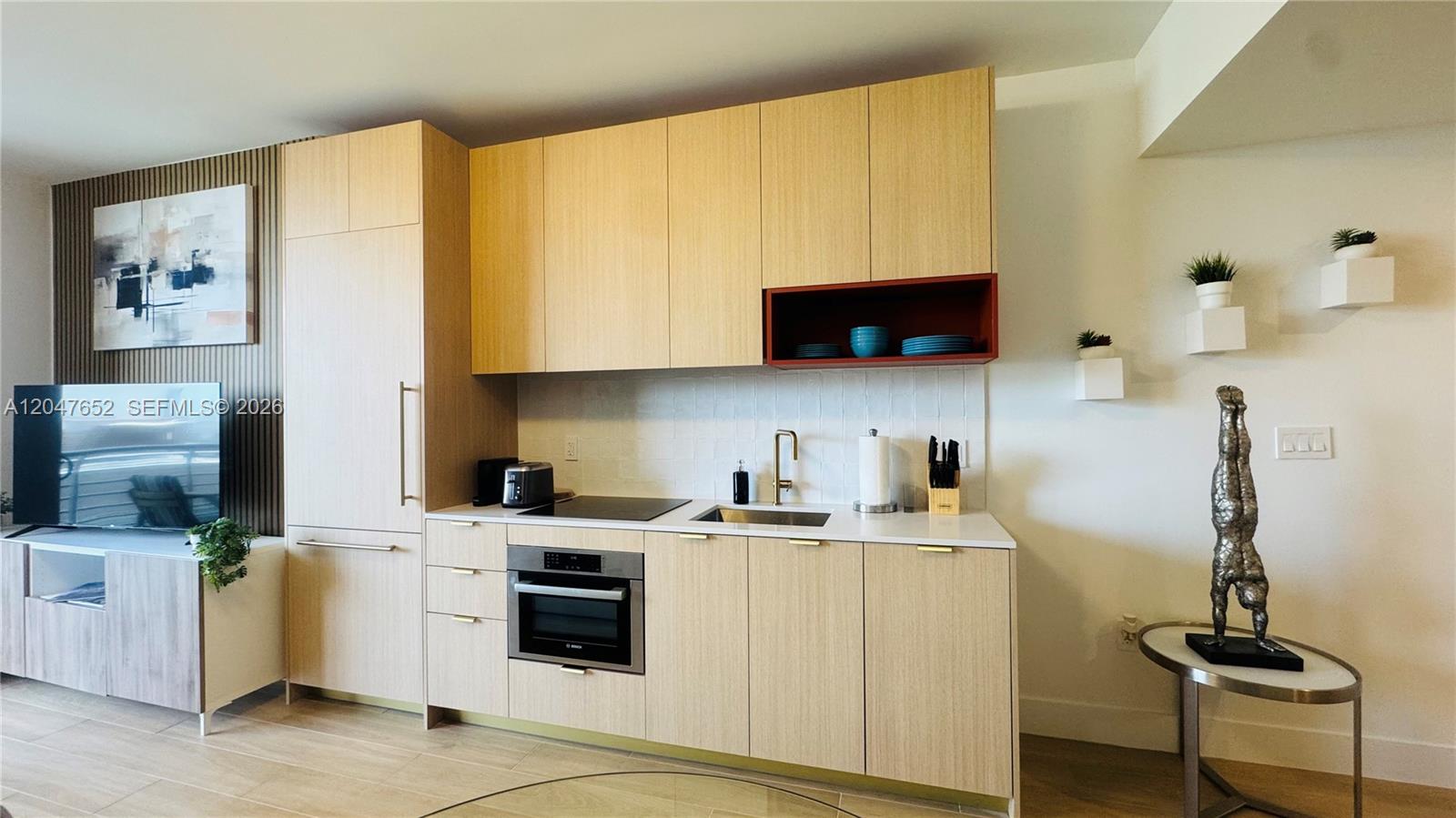 A modern kitchen features light wood cabinetry, a white countertop, and a red open shelf — 90 NE 32 St # 613, Miami FL 33137, MIAMI, FL