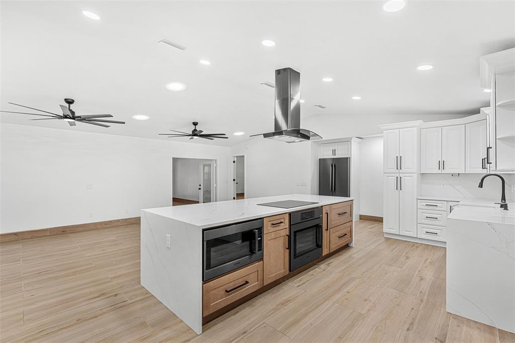 A modern kitchen features a large white quartz island with built-in appliances and wood cabinetry — 3271 MAJESTIC OAK DRIVE, ST CLOUD, FL