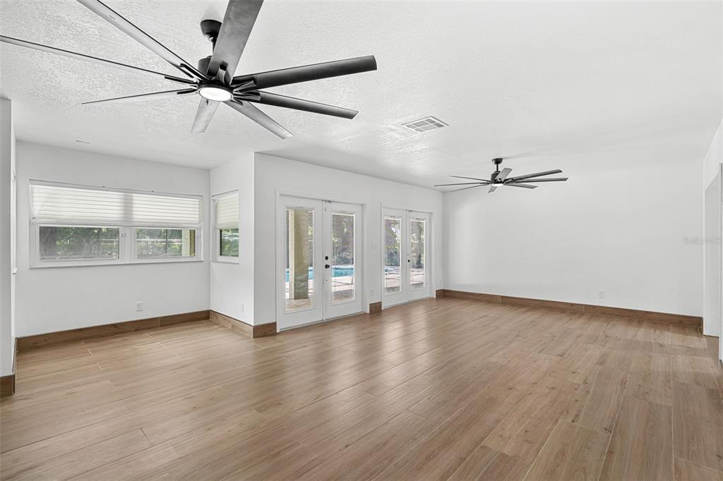 A bright, empty room features light wood-look tile flooring, two ceiling fans, and glass doors — 3271 MAJESTIC OAK DRIVE, ST CLOUD, FL