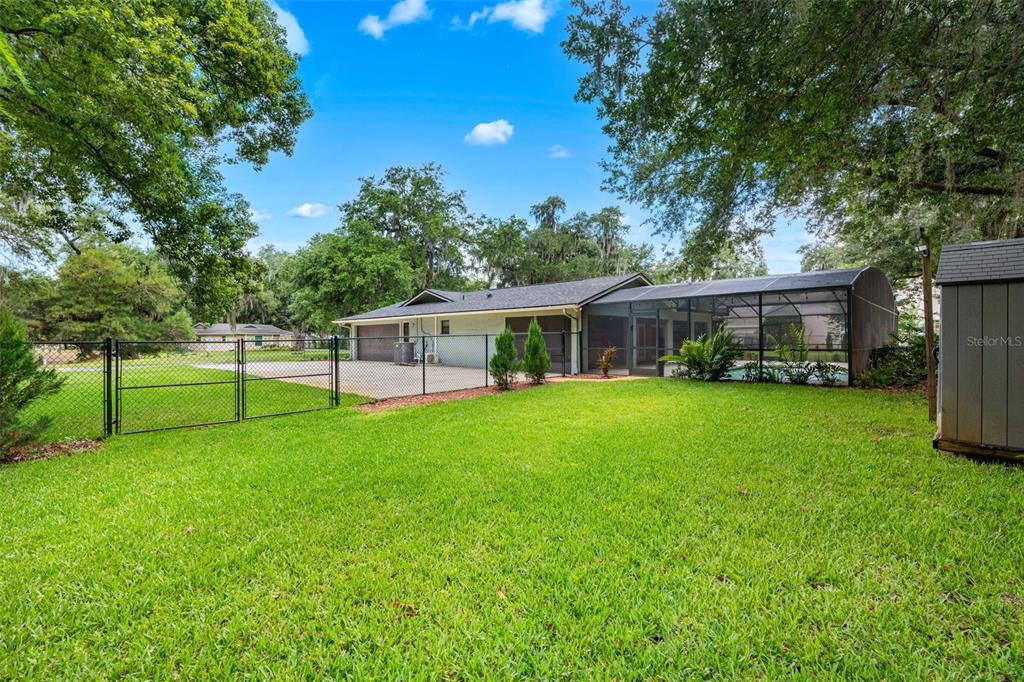 A backyard view shows a house with a screened-in pool, a driveway, and chain-link fencing — 3271 MAJESTIC OAK DRIVE, ST CLOUD, FL