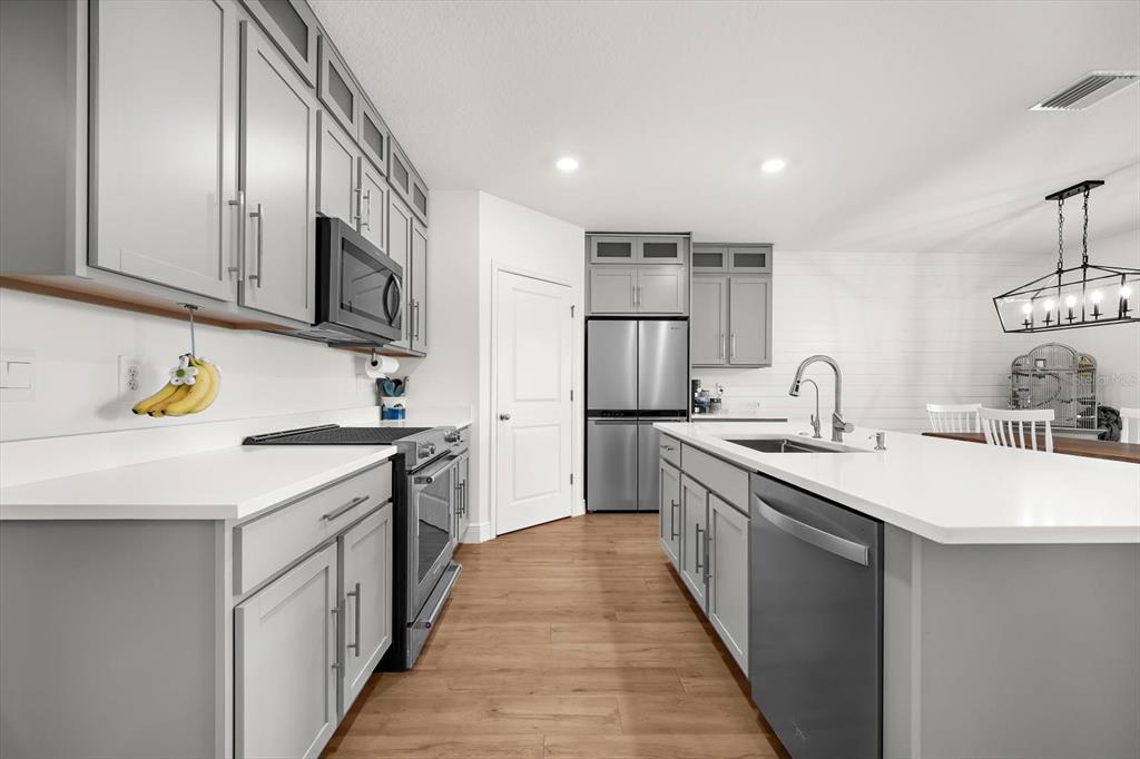 A modern kitchen features gray cabinets, white countertops, stainless steel appliances, and wood-look flooring — 17914 CANOPY PLACE, BRADENTON, FL