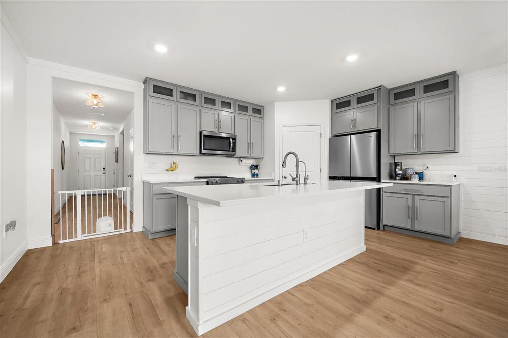 A modern kitchen features gray cabinets, white countertops, a central island, and light wood flooring — 17914 CANOPY PLACE, BRADENTON, FL