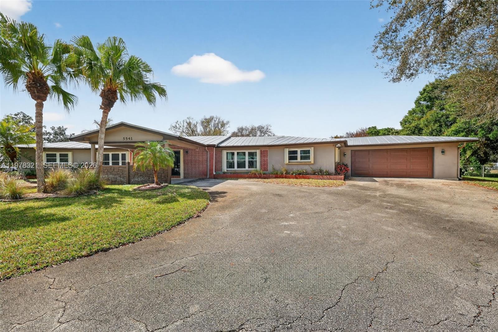 A single-story house with a metal roof, brick accents, and a large paved driveway — 5541 Teal Ter, Fort Pierce FL 34982, FORT PIERCE, FL