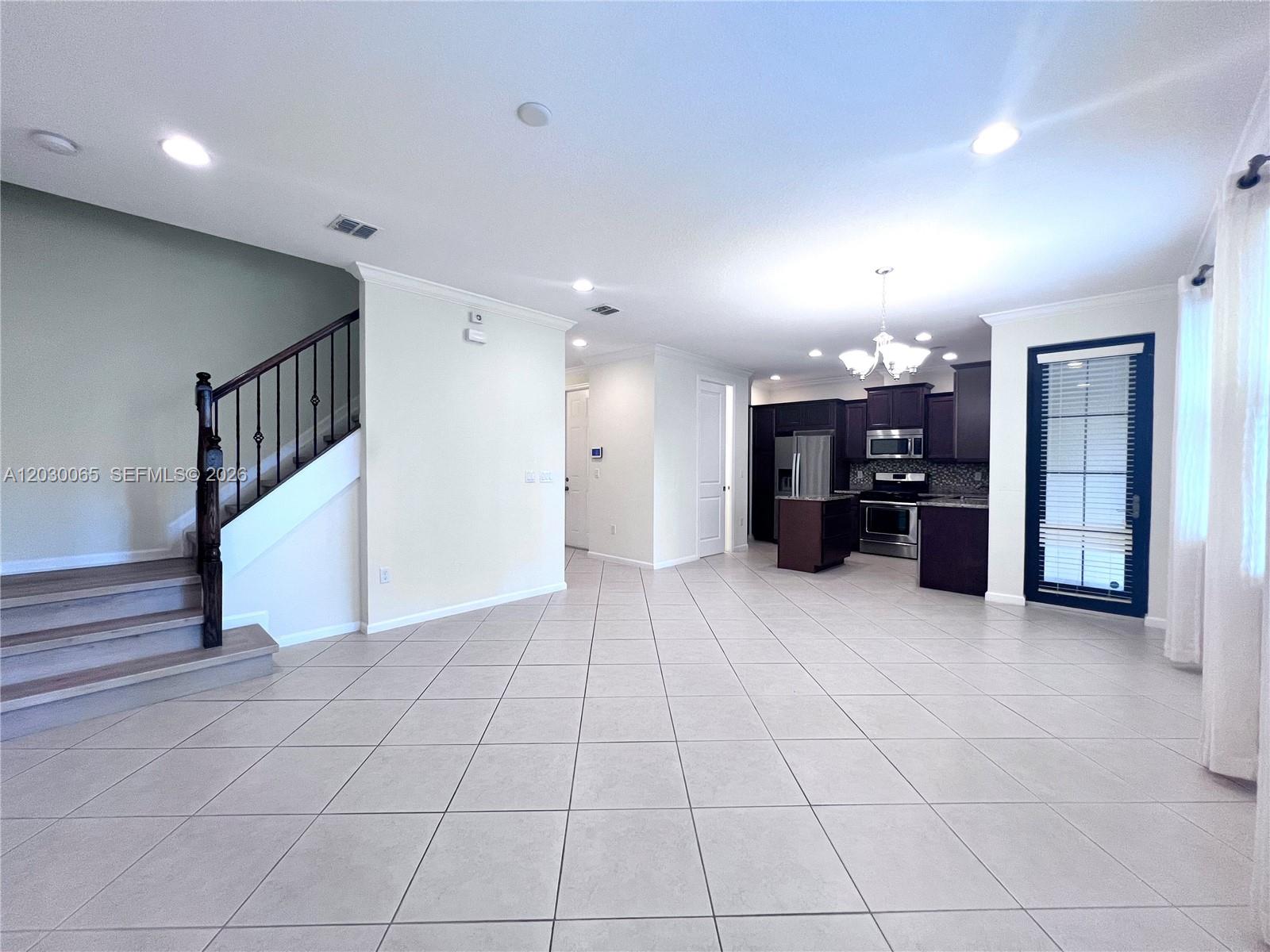 An open-concept living area features tile flooring, a staircase, and a kitchen with dark cabinetry — 3381 NW 125th Ave, Sunrise FL 33323, SUNRISE, FL