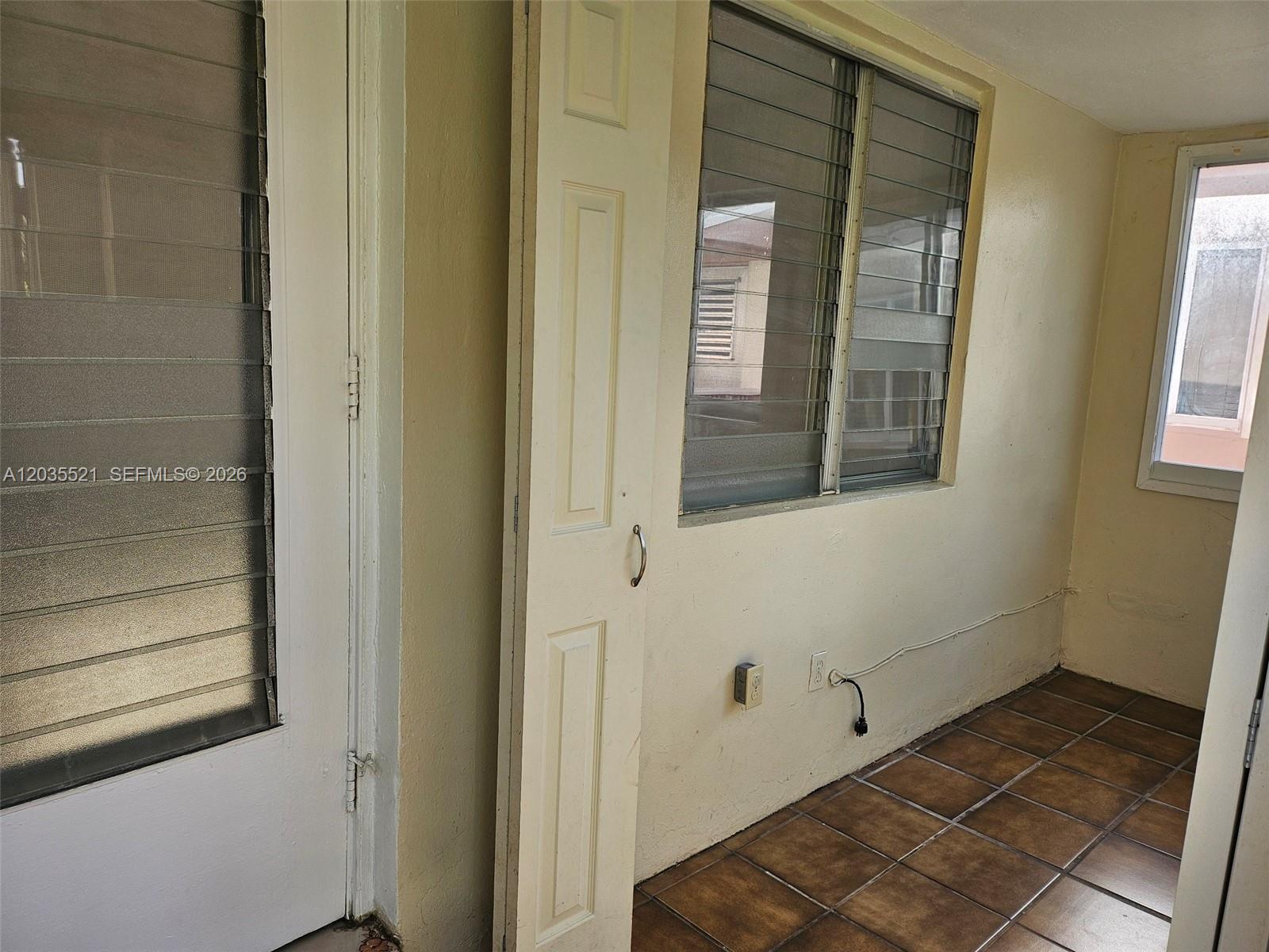A sunroom features tiled floors, beige walls, jalousie windows, and an exposed electrical outlet — 709 NE 4th Ct # 6, Hallandale Beach FL 33009, HALLANDALE BEACH, FL