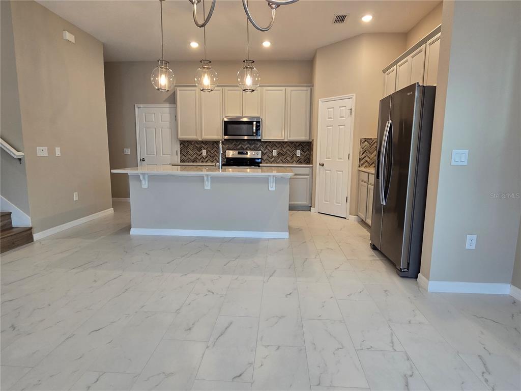 A kitchen features white cabinets, a central island, stainless steel appliances, and marble-look tile flooring — 2081 STANDING ROCK CIRCLE, WINTER GARDEN, FL