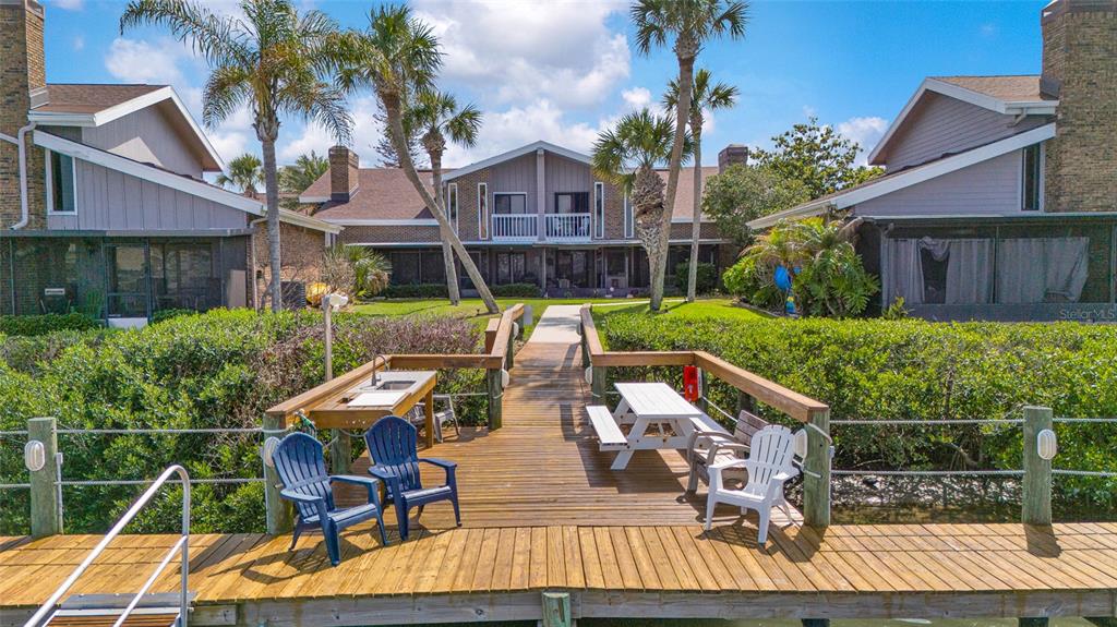 A wooden dock with a sink and seating extends toward a multi-unit residential building — 121 LAGOON COURT, NEW SMYRNA BEACH, FL