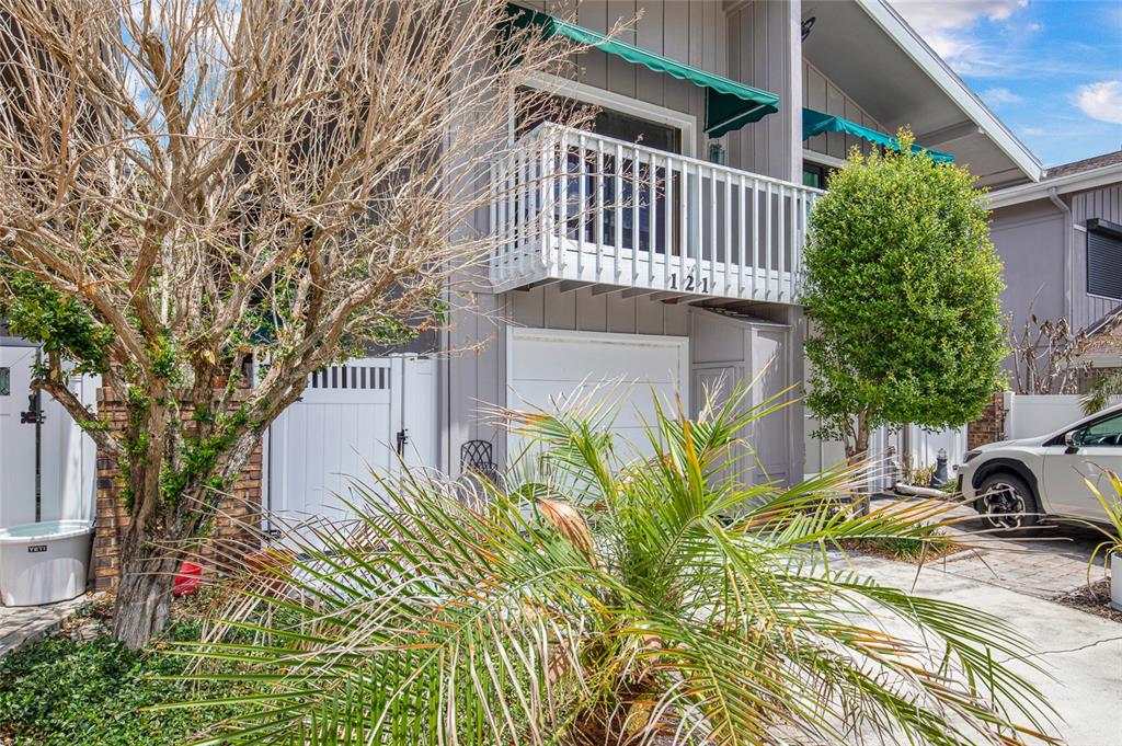 A two-story townhouse exterior features a white balcony, green awnings, and a paved driveway — 121 LAGOON COURT, NEW SMYRNA BEACH, FL