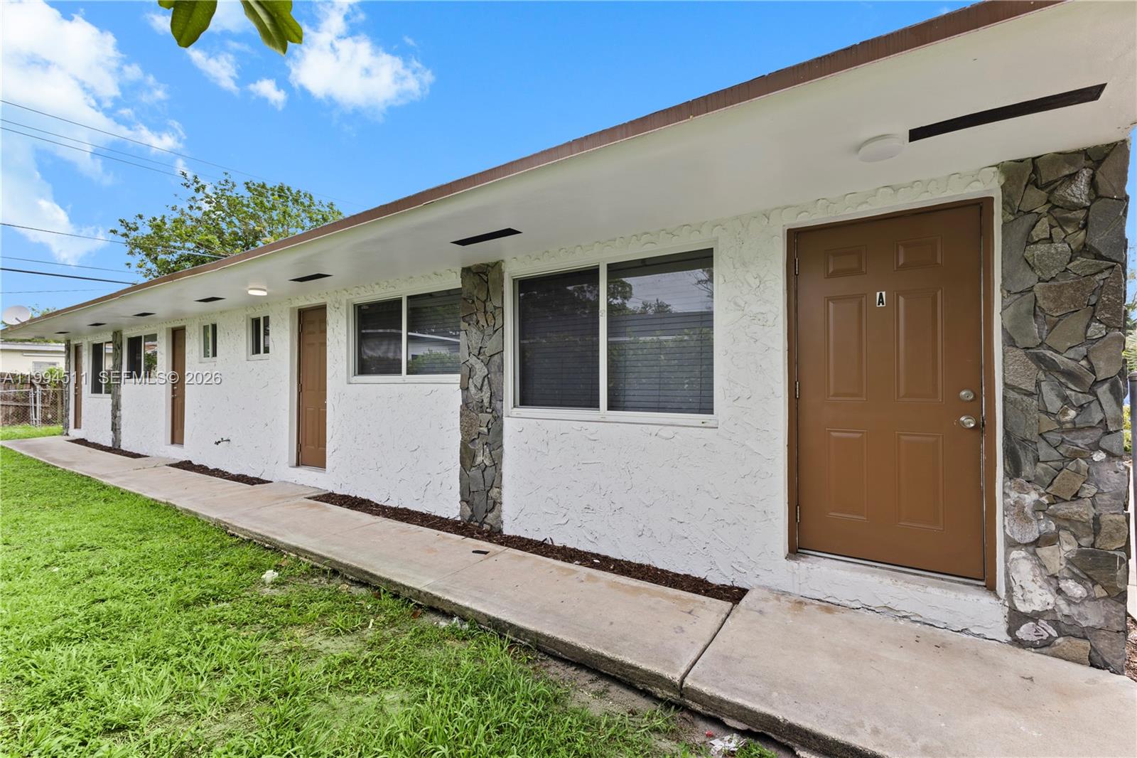 The exterior of a single-story apartment building features white stucco walls, brown doors, and stone accents — 6121 SW 40th Ct # A, Miramar FL 33023, MIRAMAR, FL