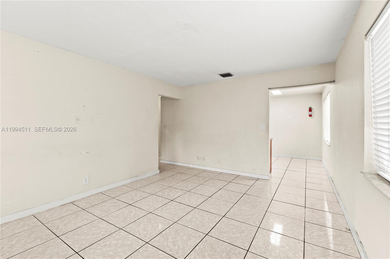 An empty room features beige tiled floors, off-white walls, and a window with blinds — 6121 SW 40th Ct # A, Miramar FL 33023, MIRAMAR, FL