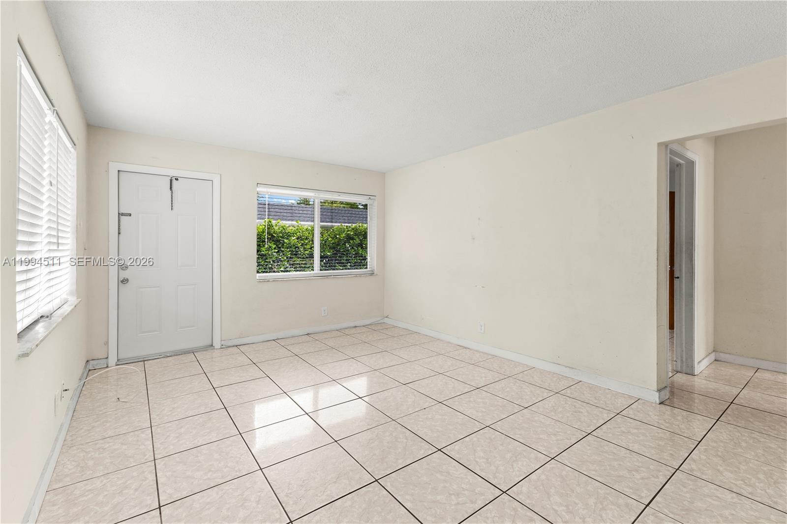 An empty room features beige tile flooring, white walls, a white door, and two windows — 6121 SW 40th Ct # A, Miramar FL 33023, MIRAMAR, FL