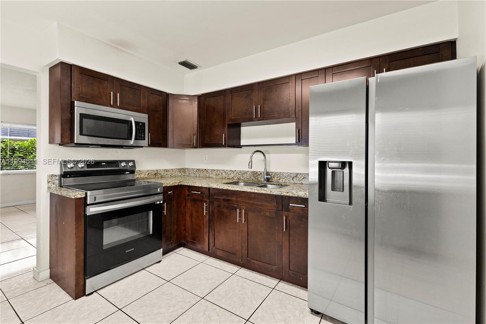 A kitchen features dark wood cabinets, granite countertops, stainless steel appliances, and light tile flooring — 6121 SW 40th Ct # A, Miramar FL 33023, MIRAMAR, FL