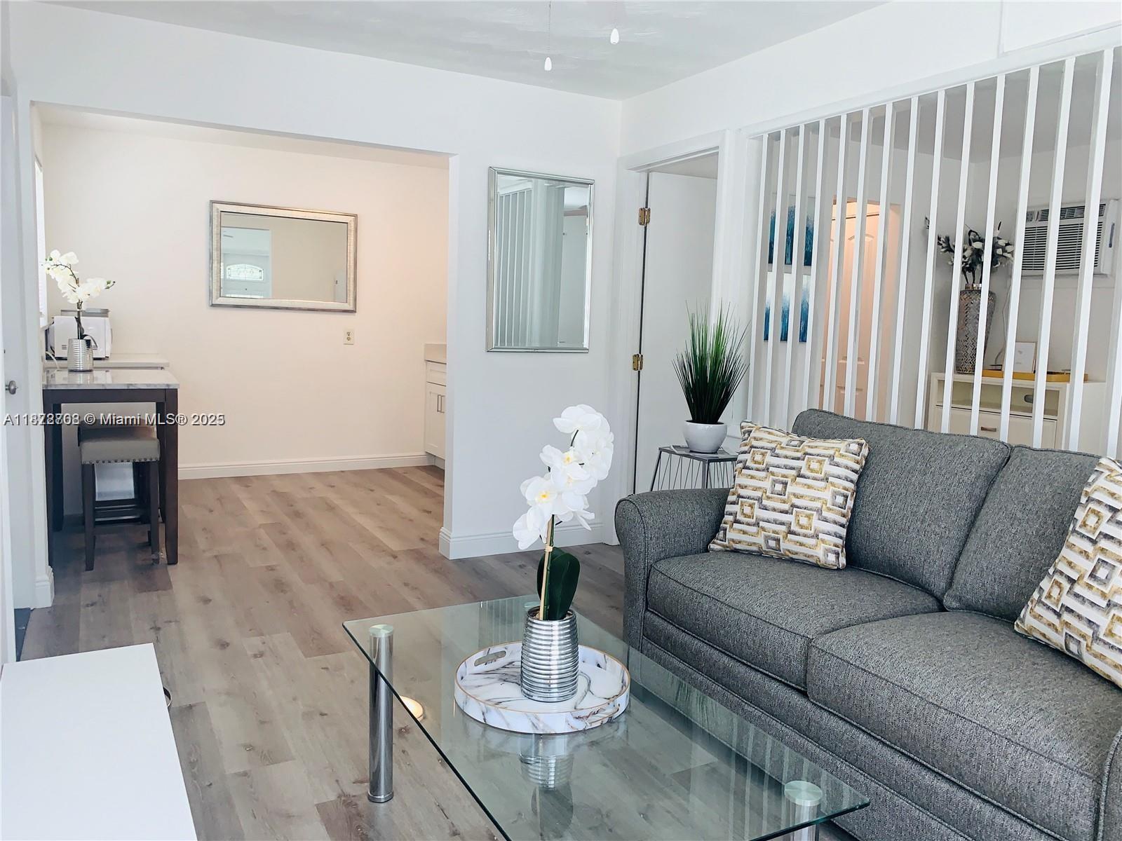 A living room features a gray sofa, glass coffee table, and light wood-look flooring — 116 SE 9th Ct, Hallandale Beach FL 33009, HALLANDALE BEACH, FL