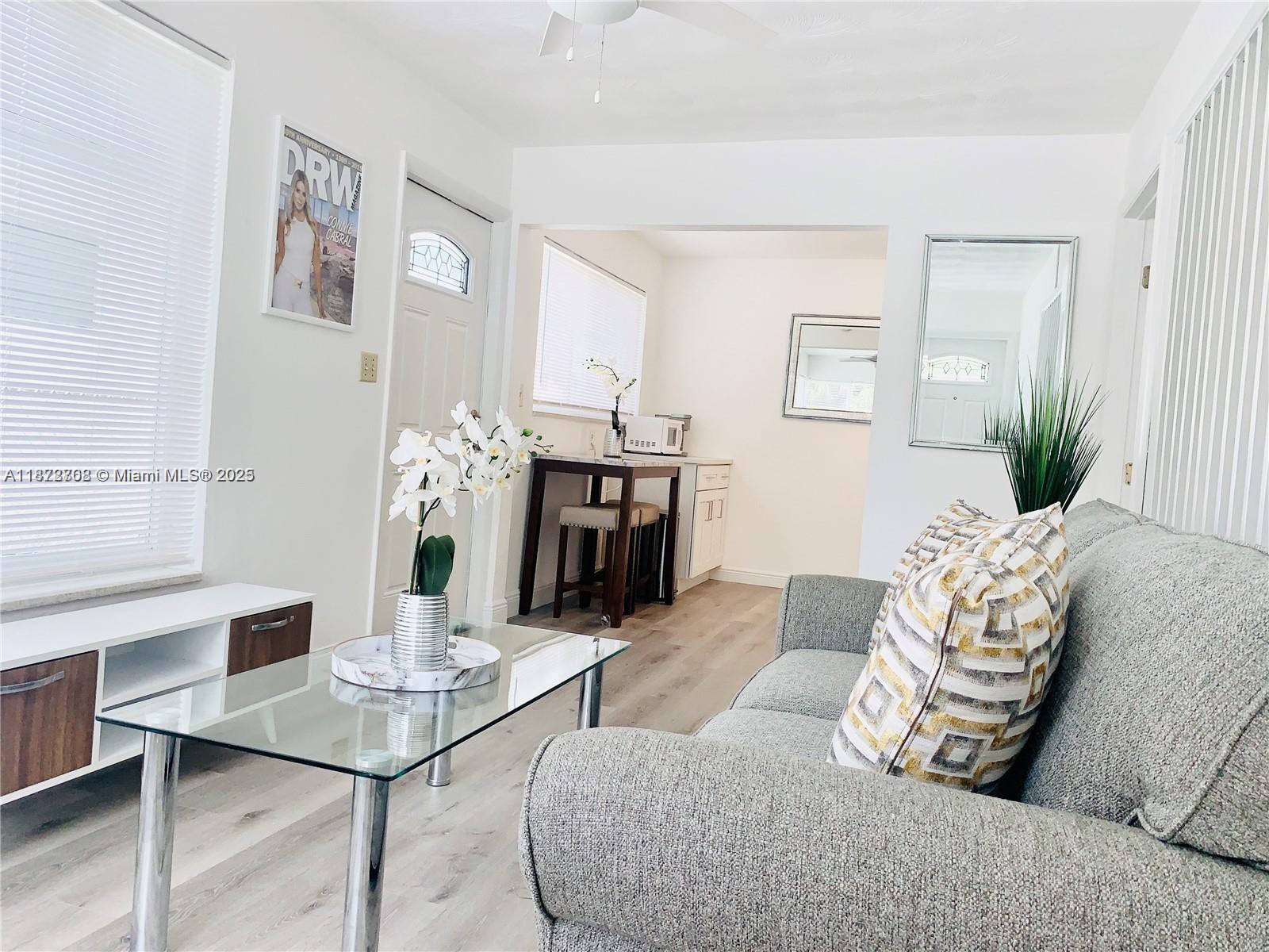 A living room features a grey sofa, glass coffee table, and an adjacent kitchen area — 116 SE 9th Ct, Hallandale Beach FL 33009, HALLANDALE BEACH, FL