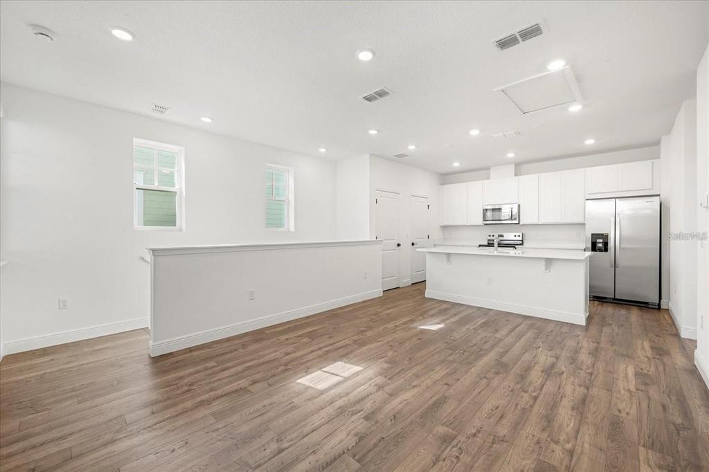 A bright, open-concept kitchen and living area with white cabinetry and wood-look flooring — 10535 MARCONI AVENUE, ORLANDO, FL