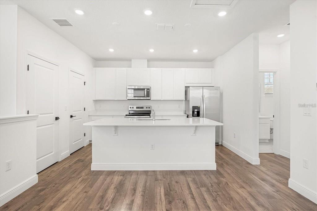 A modern kitchen features white cabinetry, stainless steel appliances, a center island, and wood flooring — 10535 MARCONI AVENUE, ORLANDO, FL