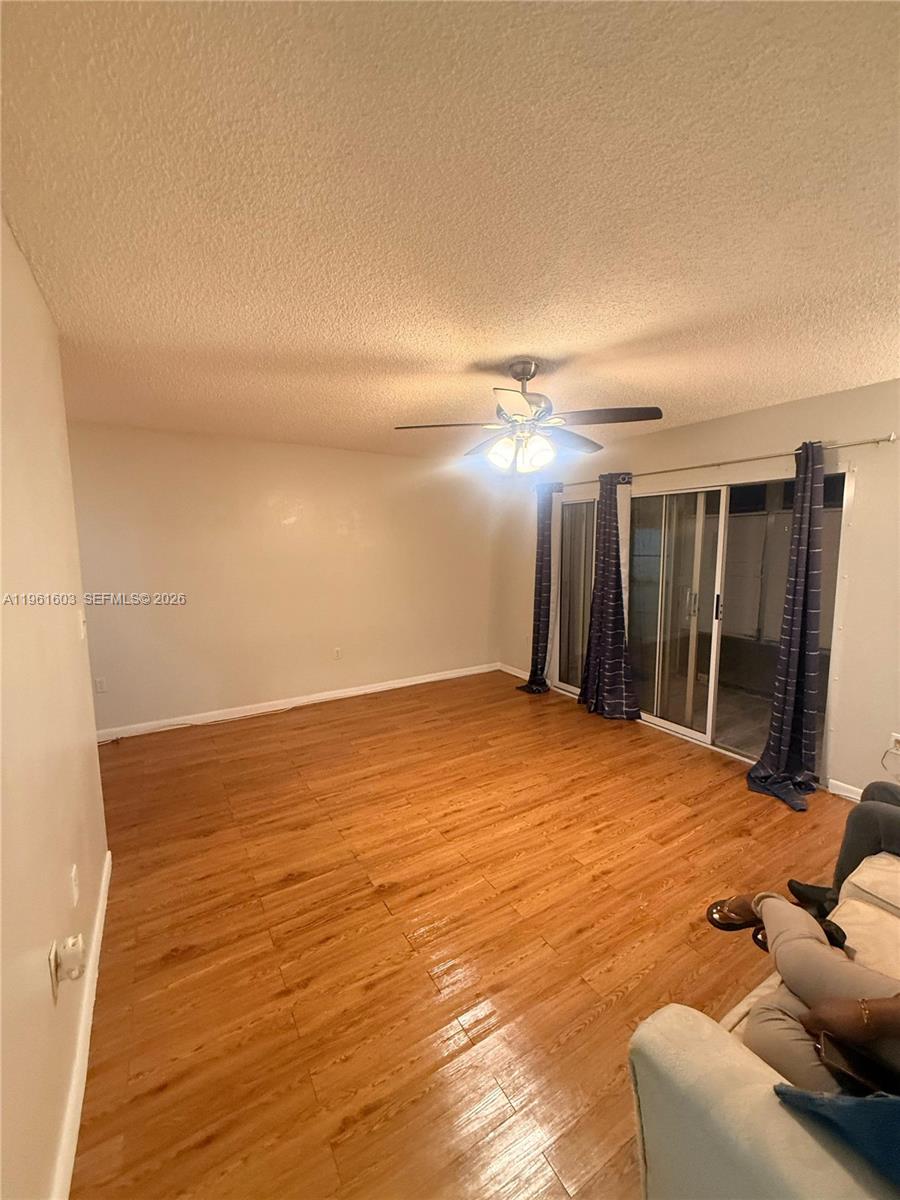 A living room features wood-look laminate flooring, a ceiling fan, and sliding glass patio doors — 5180 E Sabal Palm Blvd # 133, Tamarac FL 33319, TAMARAC, FL