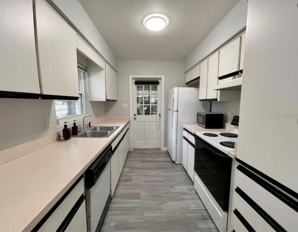 A galley kitchen features white cabinets, light countertops, stainless steel appliances, and wood-look flooring — 1751 WESTCHESTER AVENUE, WINTER PARK, FL